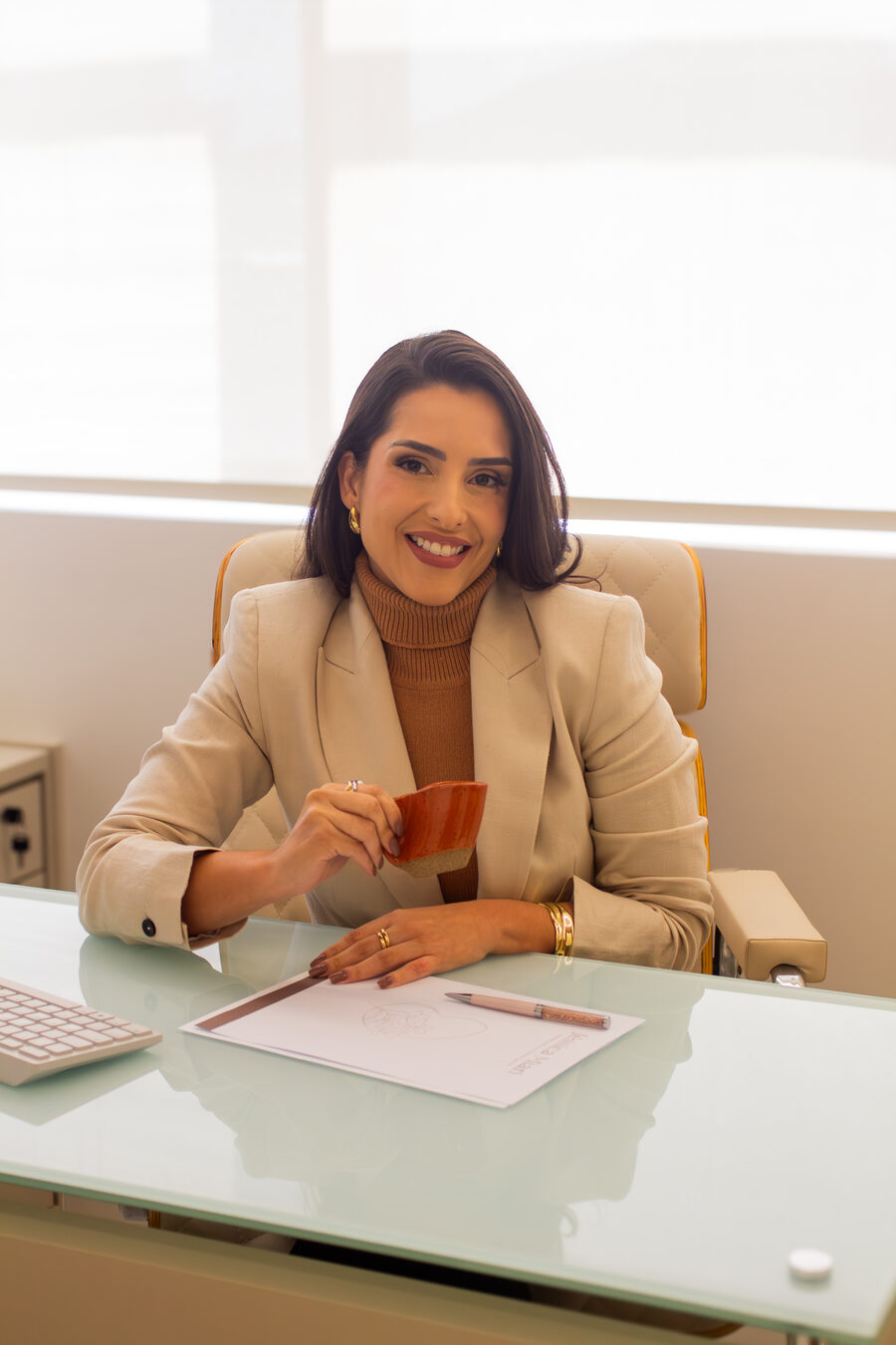 Dra. Jéssica Miari à mesa do consultório, com o computador e a papelaria da marca